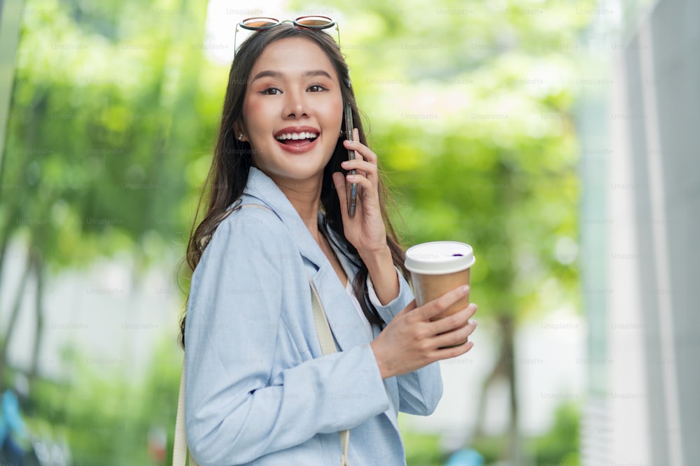 Asiatische weibliche lässige entspannen digitale Nomadin freiberufliche Expat-Programmiererin Smart Casual Tuch Gehen auf Bürgersteig Stadt mit halten Smartphone lächelnd fröhlich positives Gefühl herunterschalten Lebensstil