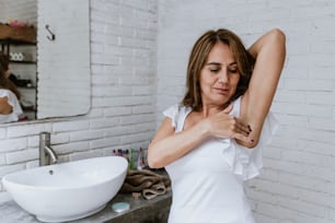Hispanic senior middle aged woman after shower using antiperspirant or deodorant after bath at home and taking care of armpit skin do daily beauty treatment in bathroom in Latin America