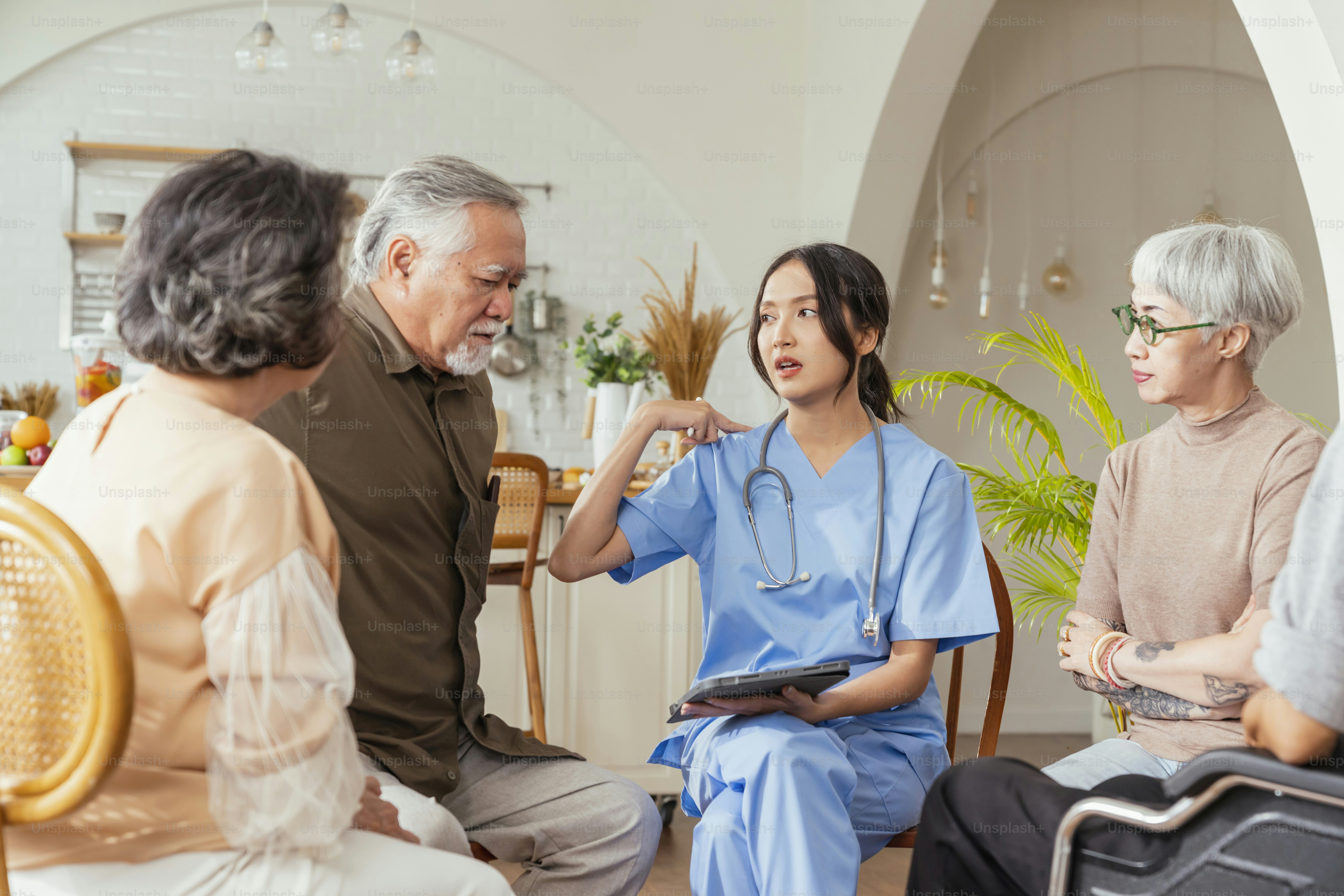happiness Cheerful elderly woman and men talking with female caregiver nurse doctor having health checking consult at living area,Caretakers with senior couple sitting in living room at nursing home