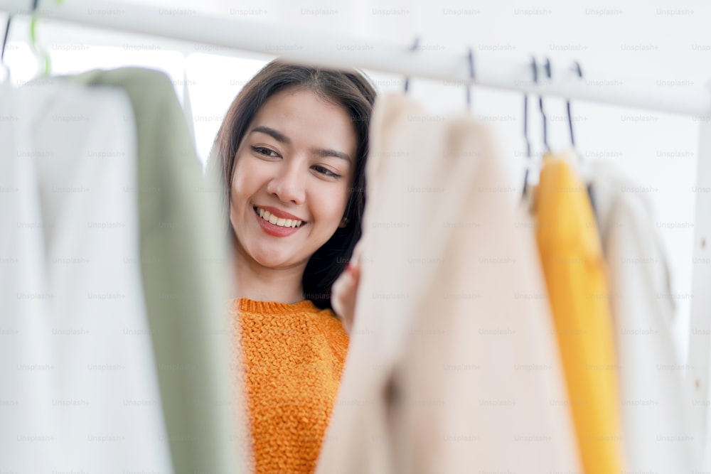똑똑한 아름다운 아시아 여성 여성은 상점 쇼핑몰에서 옷걸이에 쇼핑 천을 선택하고 소기업 소유자가 상점 비즈니스 기업가를 만들어 상점에서 옷걸이에 천을 배열하는 것을 즐깁니다.