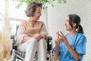 asiatique jeune soignante s’occupant de son patient âgé à la garderie pour personnes âgées Patient handicapé en fauteuil roulant à l’hôpital parlant à une infirmière amicale et regardant joyeuse infirmière roulant Patient âgé