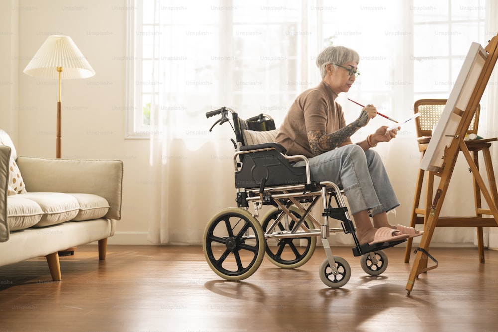 old senior asian female tattoo using art therapy while his legs is injured at home,asian elder woman spend recovering of her leg is getting better with painting canvas art in living room at home