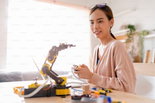 smart asian female programer learning robot arm ai coding electronic board cable in STEM, STEAM she try to testing her autonomous  robotic arm with sensors via Arduino platform at home