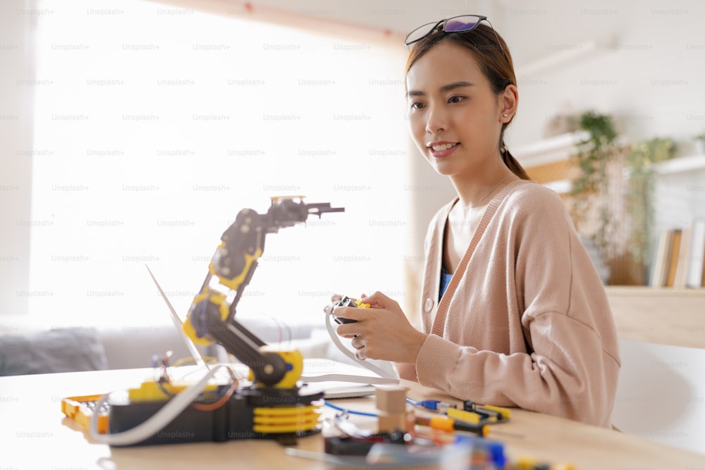 smart asian female programer learning robot arm ai coding electronic board cable in STEM, STEAM she try to testing her autonomous  robotic arm with sensors via Arduino platform at home