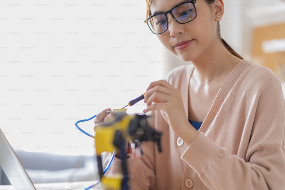 smart asian female programer learning robot arm ai coding electronic board cable in STEM, STEAM she try to testing her autonomous  robotic arm with sensors via Arduino platform at home