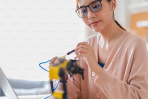 smart asian female programer learning robot arm ai coding electronic board cable in STEM, STEAM she try to testing her autonomous  robotic arm with sensors via Arduino platform at home