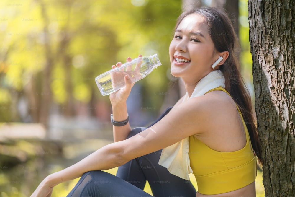 jovem Mulher bebendo água da garrafa asiática fêmea bebendo água após exercícios ou esporte. Mulher atleta bonita do fitness que bebe água pura após o exercício do exercício no treinamento esportivo matinal