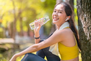 若い女性は、運動やスポーツの後にボトルのアジアの女性の飲料水から水を飲んでいます。朝のスポーツトレーニングで運動した後、純粋な水を飲む美しいフィットネスアスリートの女性
