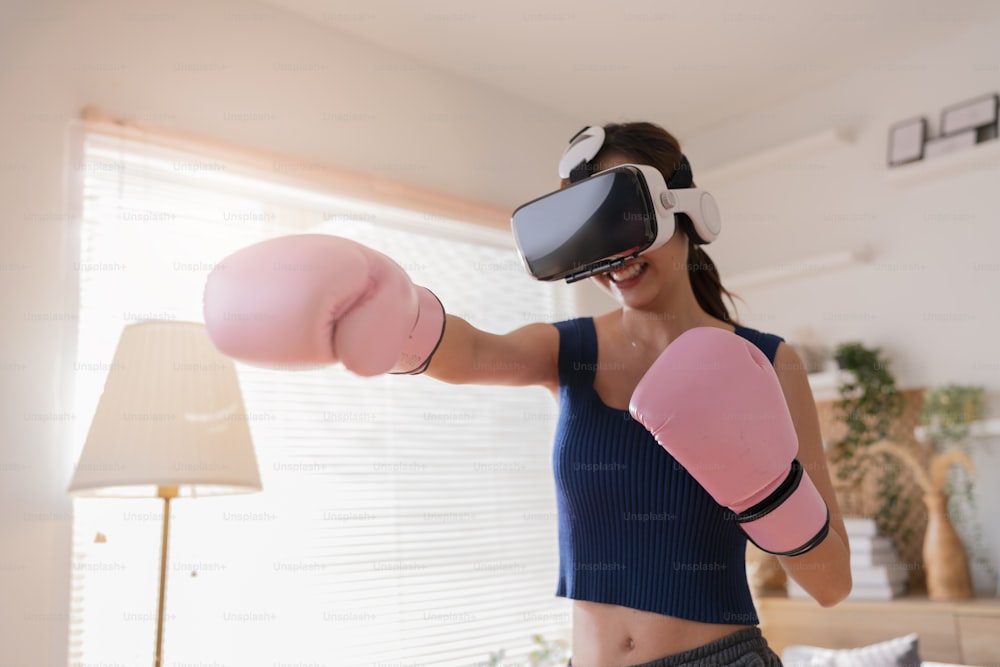 Metaverso virtuale Realtà aumentata femmina asiatica adulta che si allena boxe in cuffia VR allenamento aerobico per pugilato pugno in realtà virtuale in soggiorno sfondo interno casa