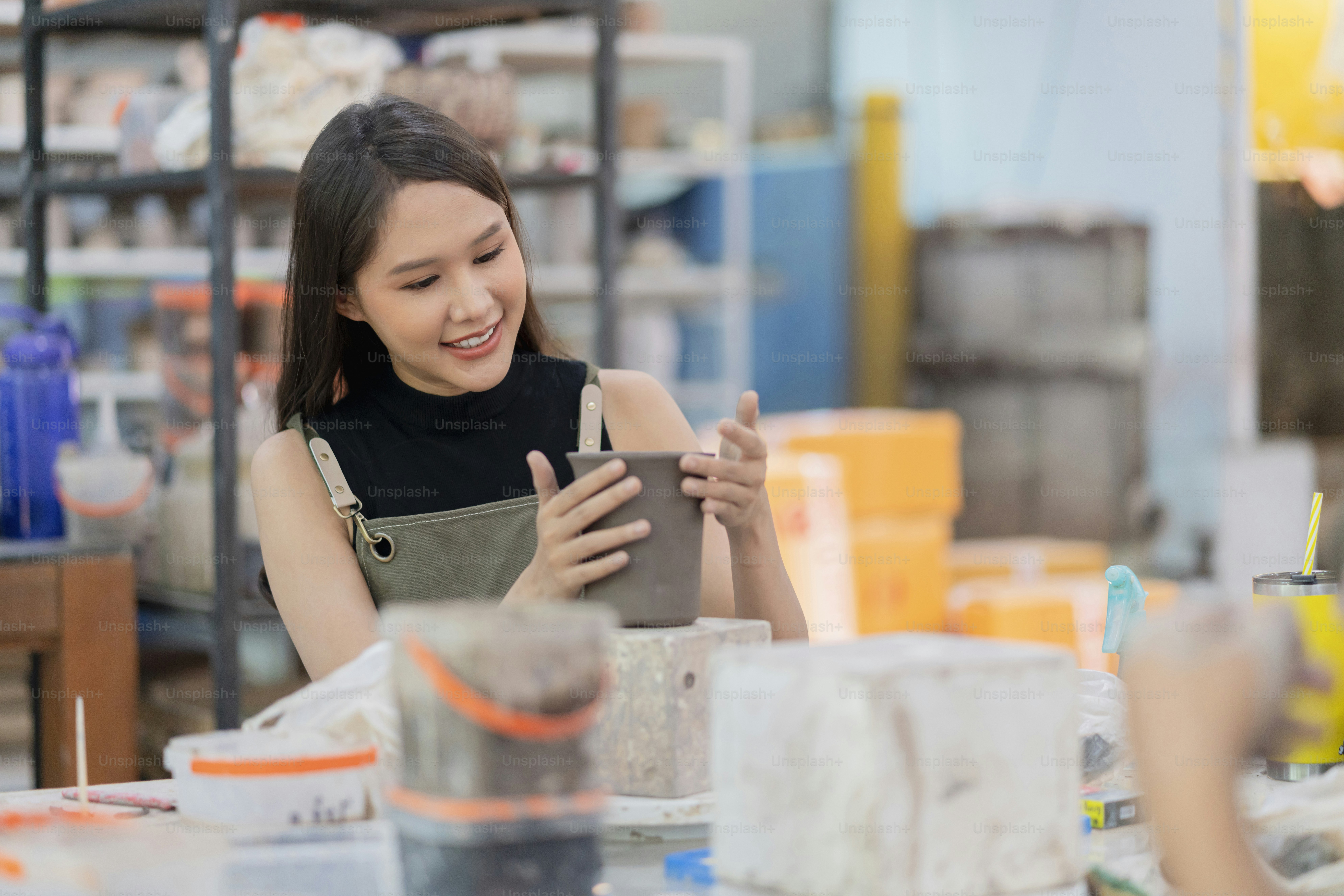 Asian Young woman female artist wear apron making clay vase bowl Beautiful young sculptor creates a clay art vase in home studio warehouse,Ceramist artist female work in studio