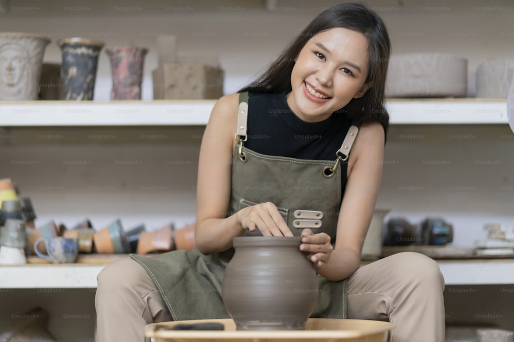 도공 바퀴에서 일하는 여성 손의 클로즈업, 집에서 도공의 바퀴에 곰팡이 작은 꽃병 그릇 점토를 형성하는 아시아 여성 조각 여성 스튜디오 워크샵 예술 및 창조 취미 개념