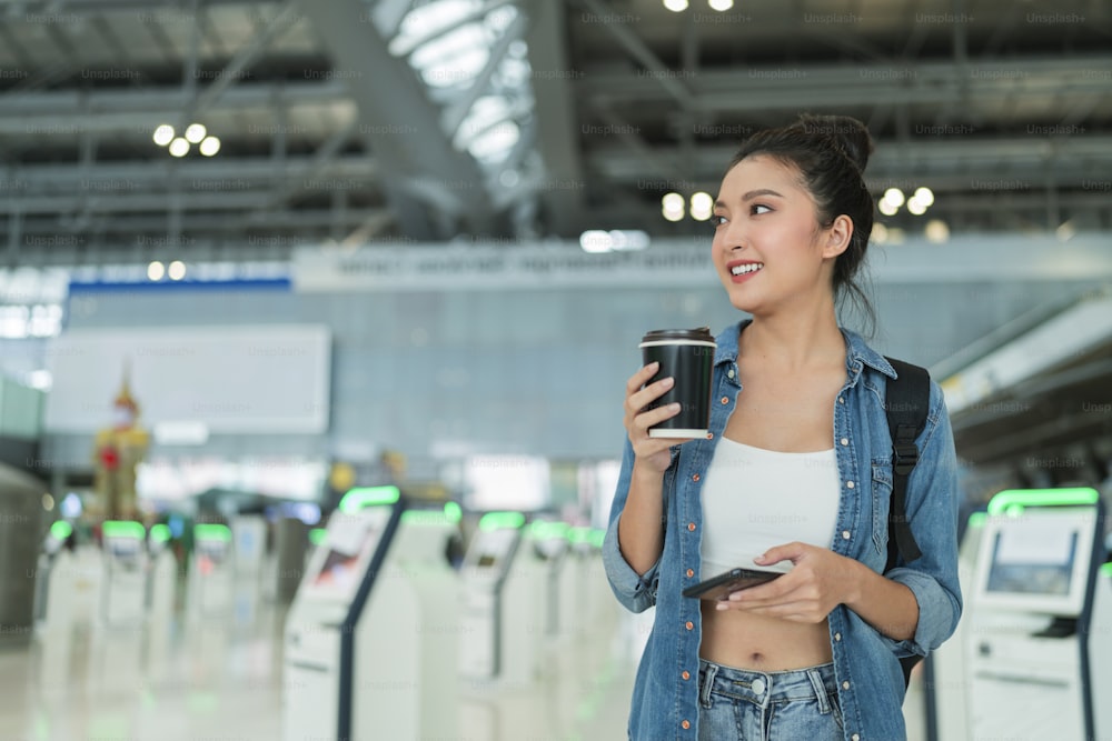 Expatriado nómada digital de viajes y trabajo, asiático alegre femenino casual que camina con la ropa casual mientras usa la aplicación de información de boletos en línea de registro de vuelo de reserva de teléfono inteligente en el concepto de viaje de la terminal del aeropuerto