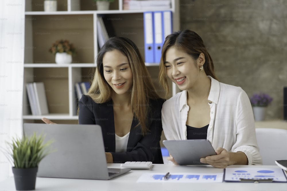 Two young Asian professional businesswomen working talking in a modern startup with laptop computer at the office.