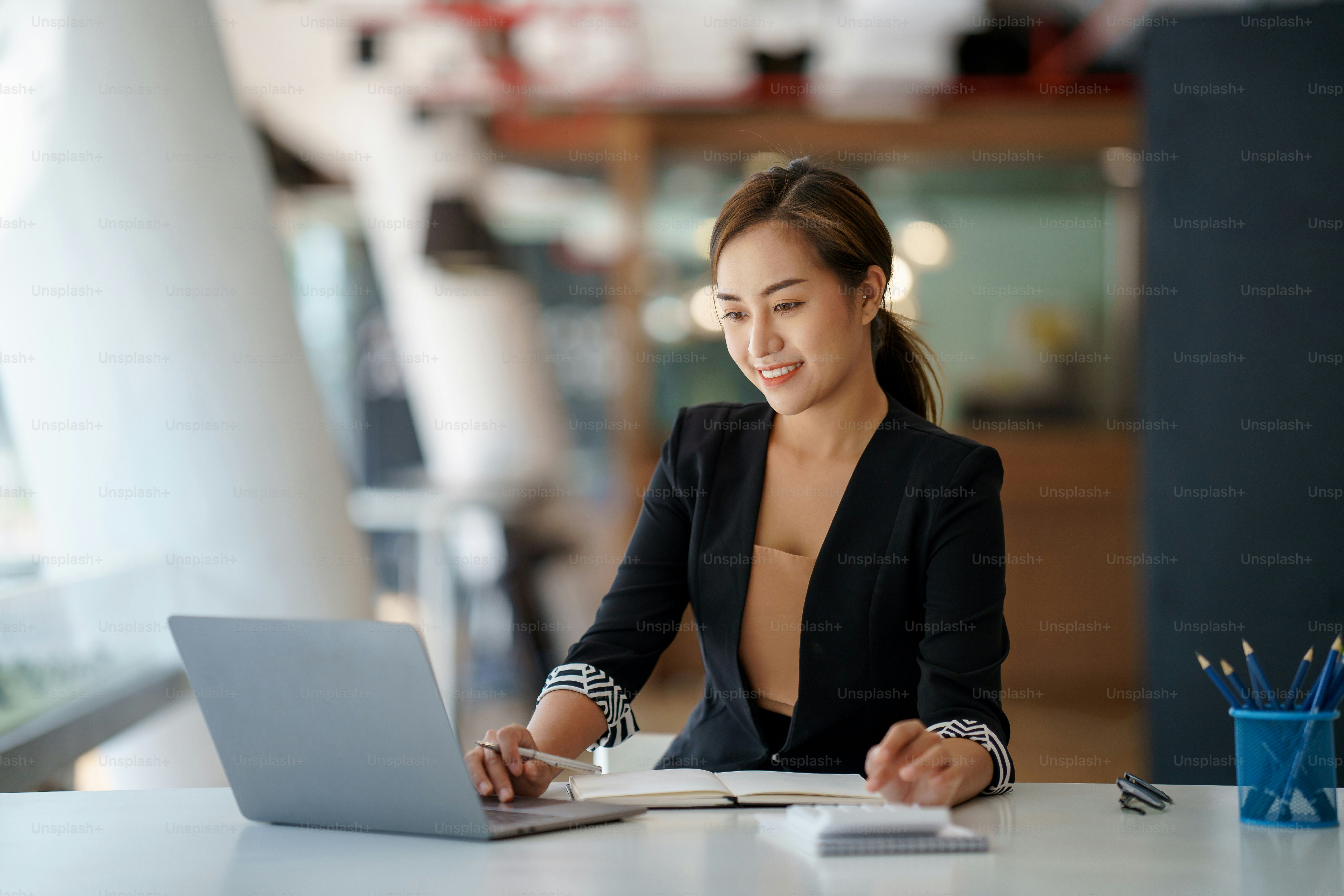 Asian businesswoman sitting happily working on her laptop in the office.