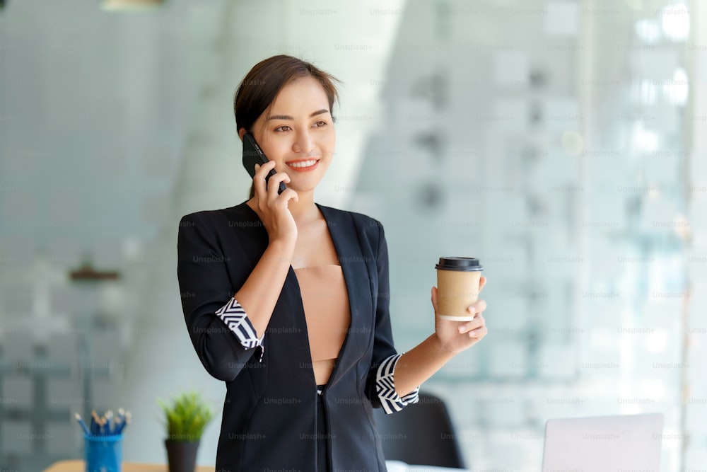 Pretty young Asian business woman standing talking on the phone in the office.