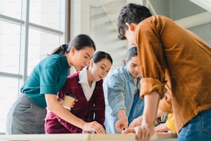 Asian businessmen and businesswomen meeting brainstorming ideas about creative web design planning application and developing template layout for mobile phone project working together in small office.