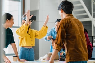 Hombres y mujeres de negocios asiáticos que se reúnen para intercambiar ideas utilizando gafas de realidad virtual (realidad virtual) que prueban la aplicación móvil de desarrollar software que trabajan juntos en la oficina moderna. Concepto de trabajo en equipo de compañeros de trabajo