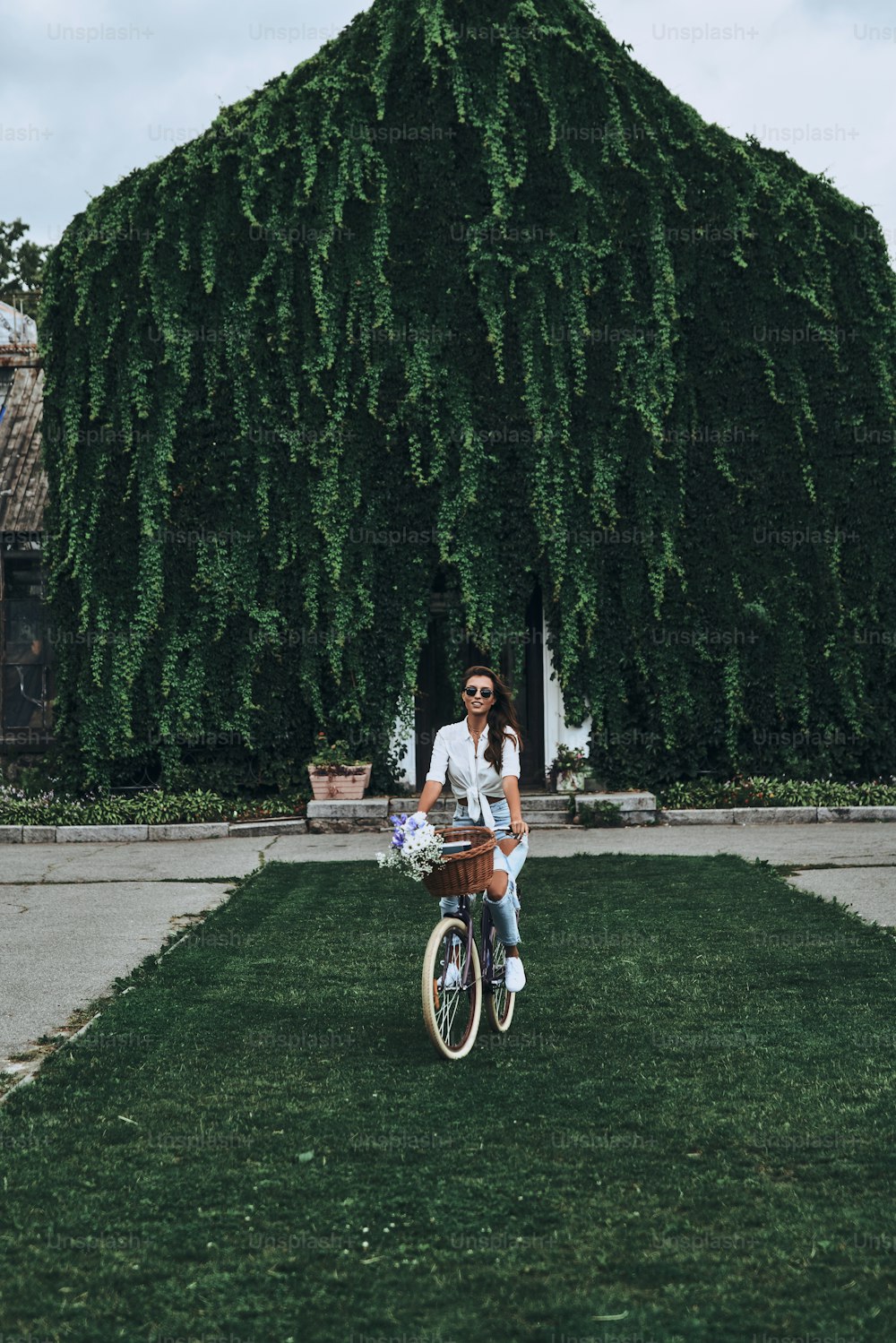 Full length of attractive young woman in casual wear spending carefree time while cycling in front of the house covered with ivy
