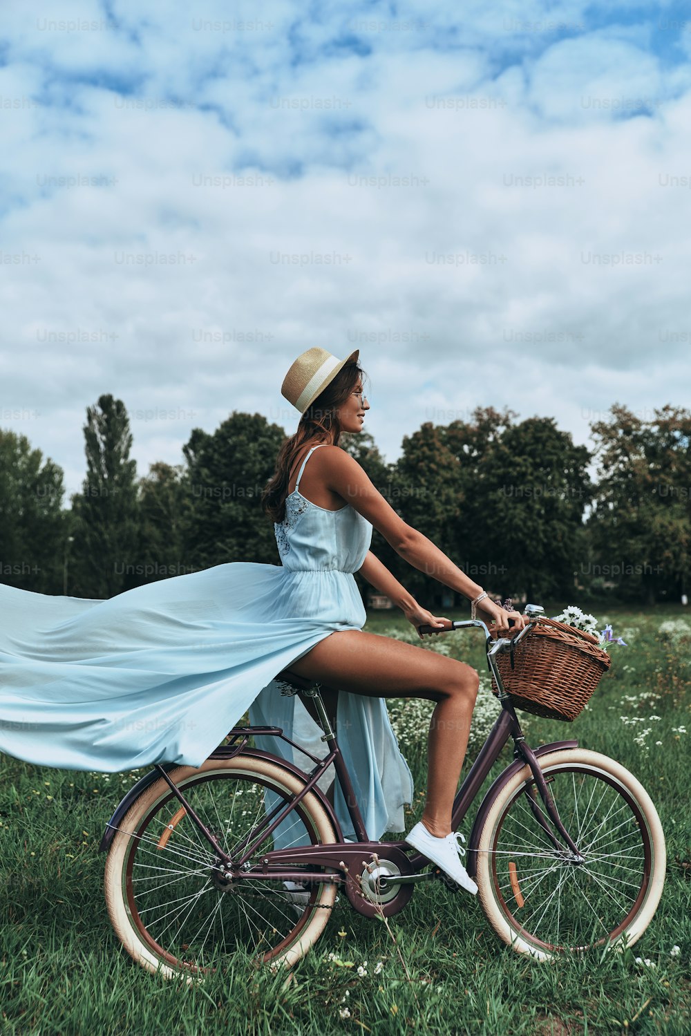 Full length of attractive young woman in dress smiling while riding on her old fashioned bicycle through the meadow