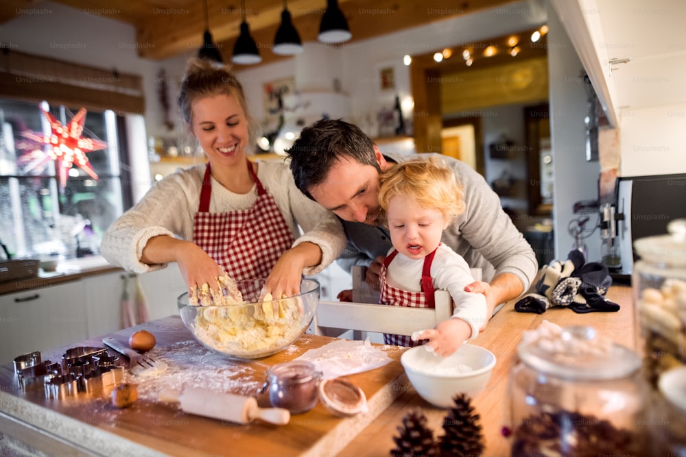 Woman, man and toddler boy making cookies at home. Mother, father and son baking gingerbread Christmas cookies.