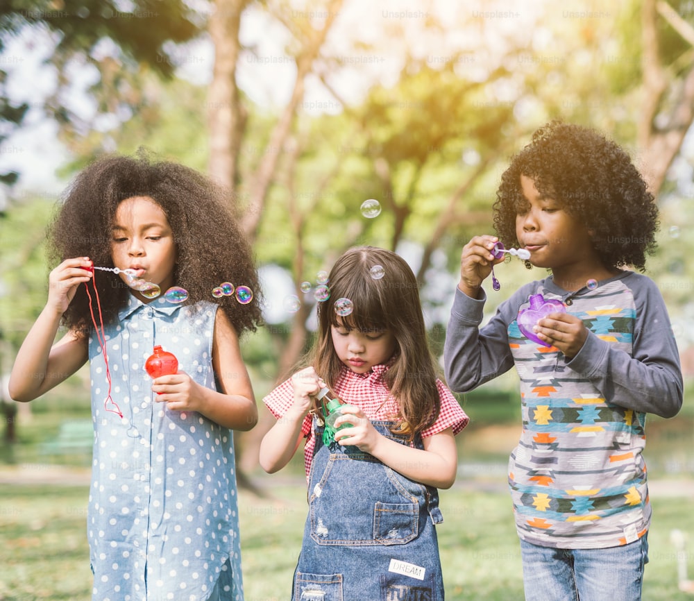 Group of Diverse Kids cute friends having bubble fun on green lawn in park