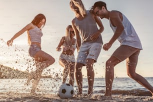 Gruppo di giovani amici attraenti si divertono sulla spiaggia e giocano a calcio