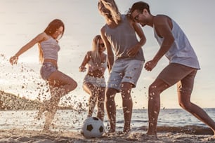 Group of young attractive friends are having fun on beach and playing football