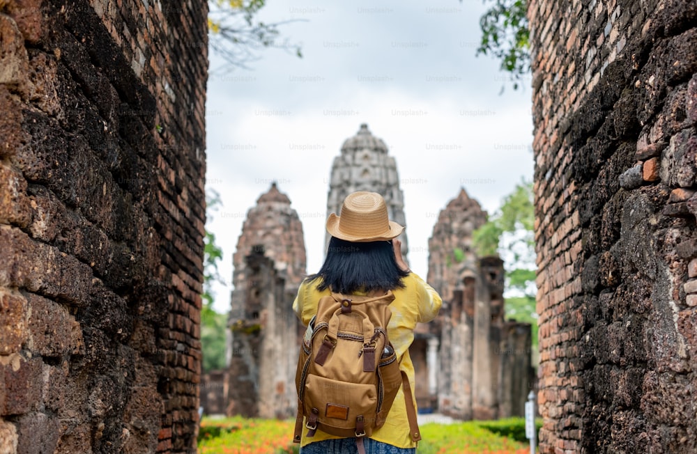 Asian tourist woman take a photo of ancient of pagoda temple thai architecture at Sukhothai,Thailand. Female traveler in casual thai cloths style visiting city concept