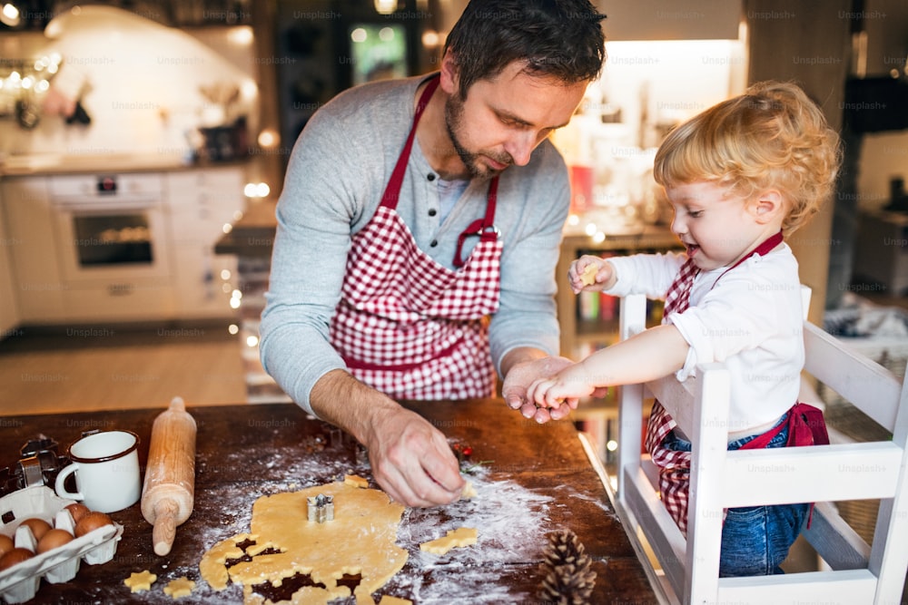 家でクッキーを作る男と幼児の男の子。ジンジャーブレッドのクリスマスクッキーを焼く父と息子。
