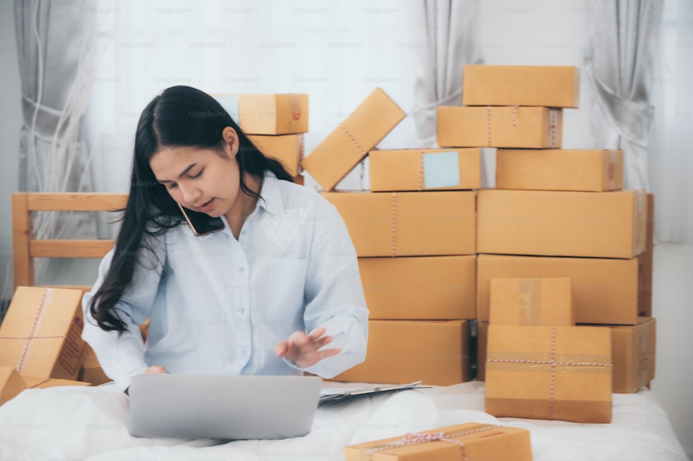 Asian women black hair in white t-shirt business owner working at home with packing box on workplace - online shopping SME entrepreneur or online selling concept. work at home concept, white background. pick up phone and taking order