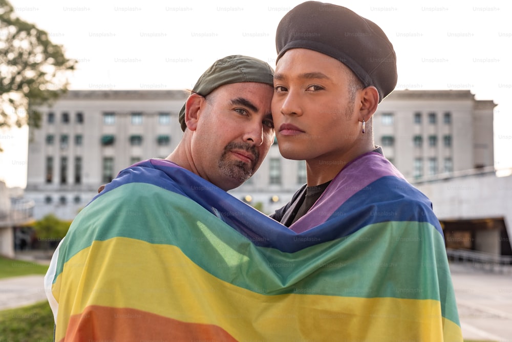 Coppia gay sotto la bandiera arcobaleno LGBT mentre guarda la macchina fotografica. Concetto di orgoglio. Mese dell'orgoglio.