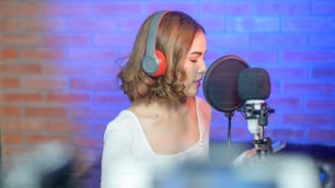 Uma jovem cantora sorridente usando fones de ouvido com microfone enquanto gravava música em um estúdio de música com luzes coloridas.