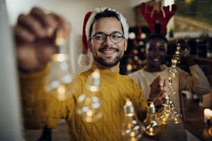 Giovane uomo felice e la sua ragazza che fanno i preparativi per la festa di Natale e decorano la loro casa con ghirlanda luminosa.