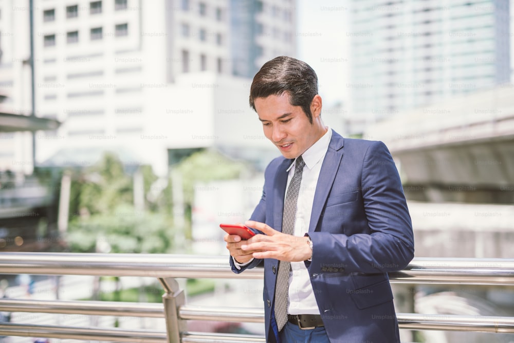 Homme d’affaires asiatique parlant en lisant son téléphone intelligent.