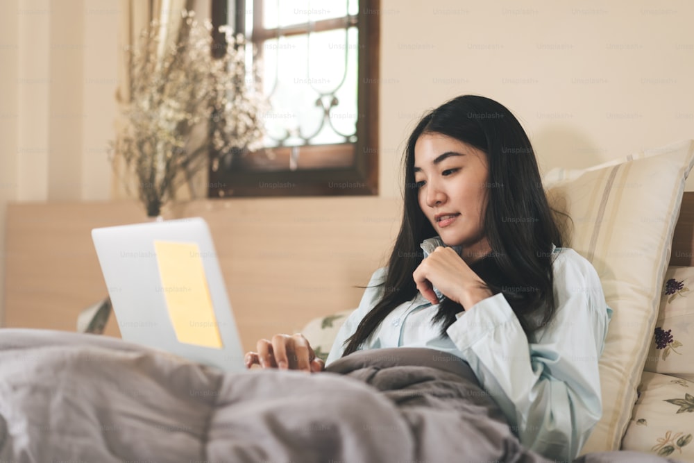 Lifestyle routine with internet technology concept. Young adult asian woman using laptop on bed for telemedicine mental health or shopping online. People rest in bedroom activity.