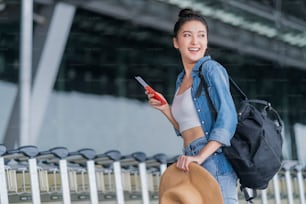 sonriente mujer asiática relajarse despreocupada ropa casual caminando en el aeropuerto mano sostener la tarjeta de embarque y la bolsa de equipaje viajes de verano vacaciones estilo de vida, asia nómada digital expatriado trabajo y viajes