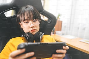 Mujer gamer asiática adulta joven estilo nerd usa anteojos y auriculares juega un juego en línea. Competencia por el estado de ánimo de la victoria. Estilo de vida de ocio de la gente en casa.