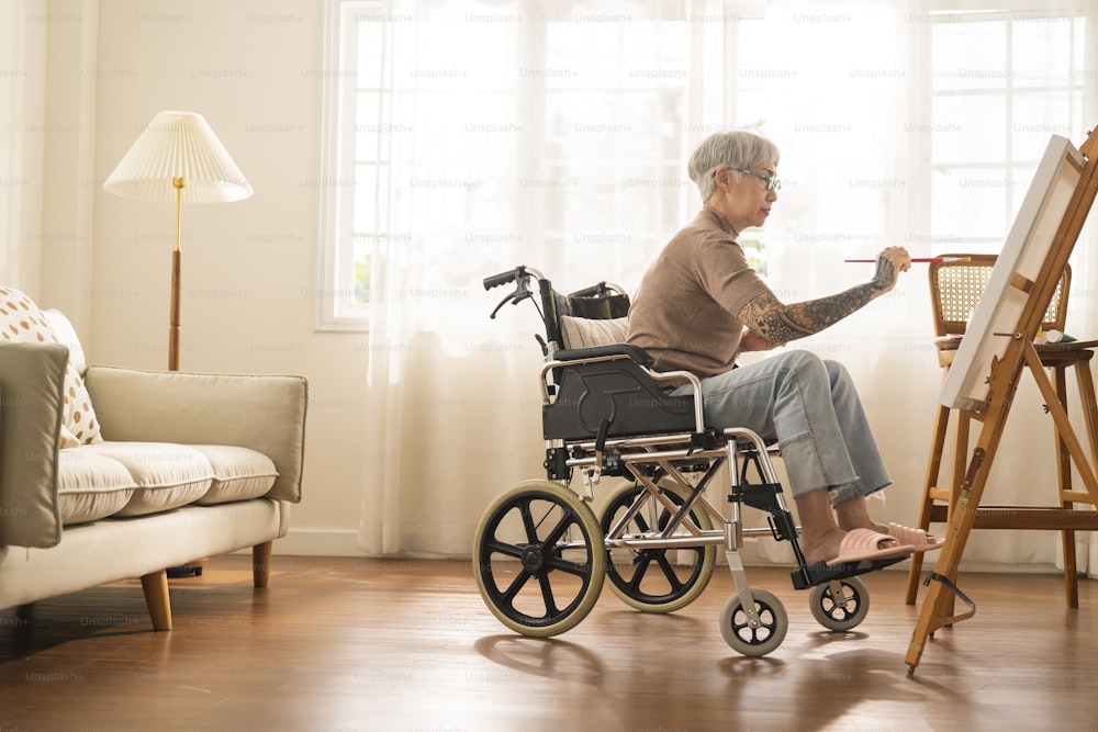 old senior asian female tattoo using art therapy while his legs is injured at home,asian elder woman spend recovering of her leg is getting better with painting canvas art in living room at home