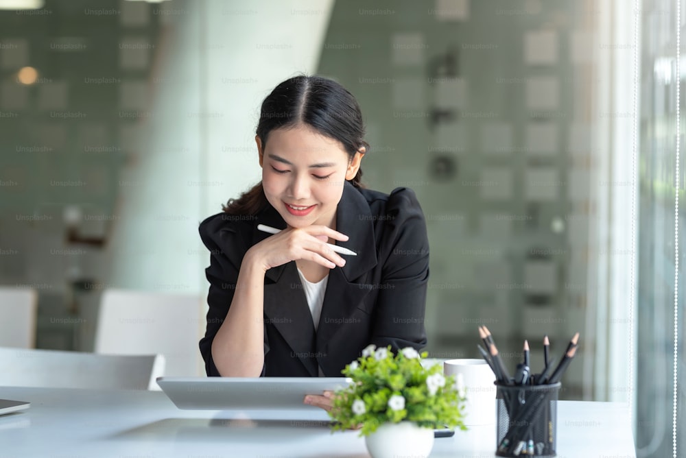 Beautiful young Asian businesswoman smiling sitting working on tablet in office.