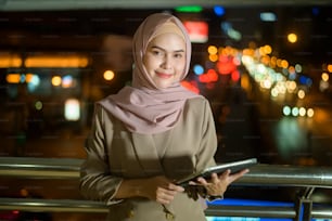 Una giovane donna d'affari musulmana sta usando il computer della compressa nella città moderna di notte, concetto di stile di vita della tecnologia di affari