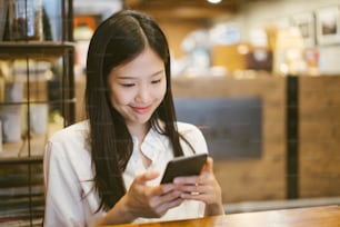 Young Asian woman using phone at a coffee shop happy and smile.