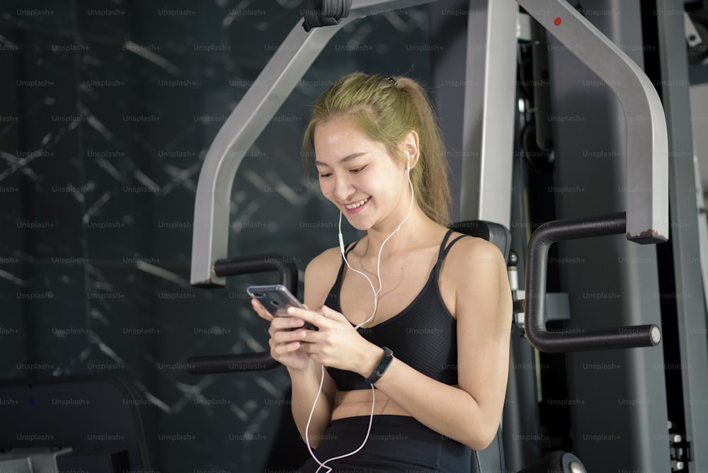 Eine schöne lächelnde Frau in Kopfhörern, die ein soziales Netzwerk nutzt und Musik im Fitnessstudio hört, Fitness- und Technologiekonzept