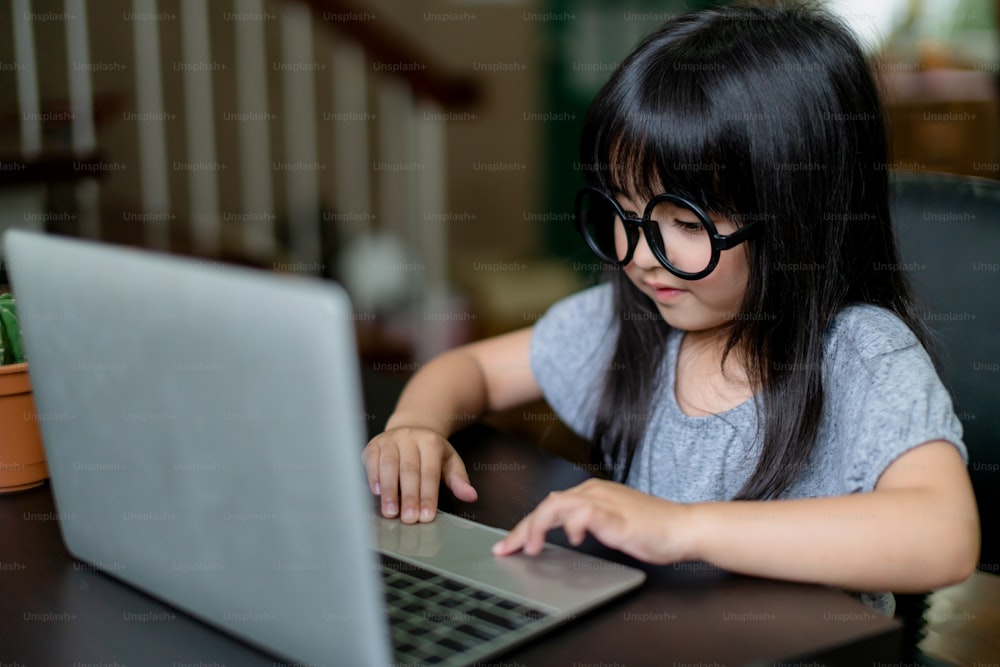 Kleine entzückende Tochter tragen Brille haben Spaß beim Spielen Laptop Pretenting Arbeit zu Hause Hintergrund