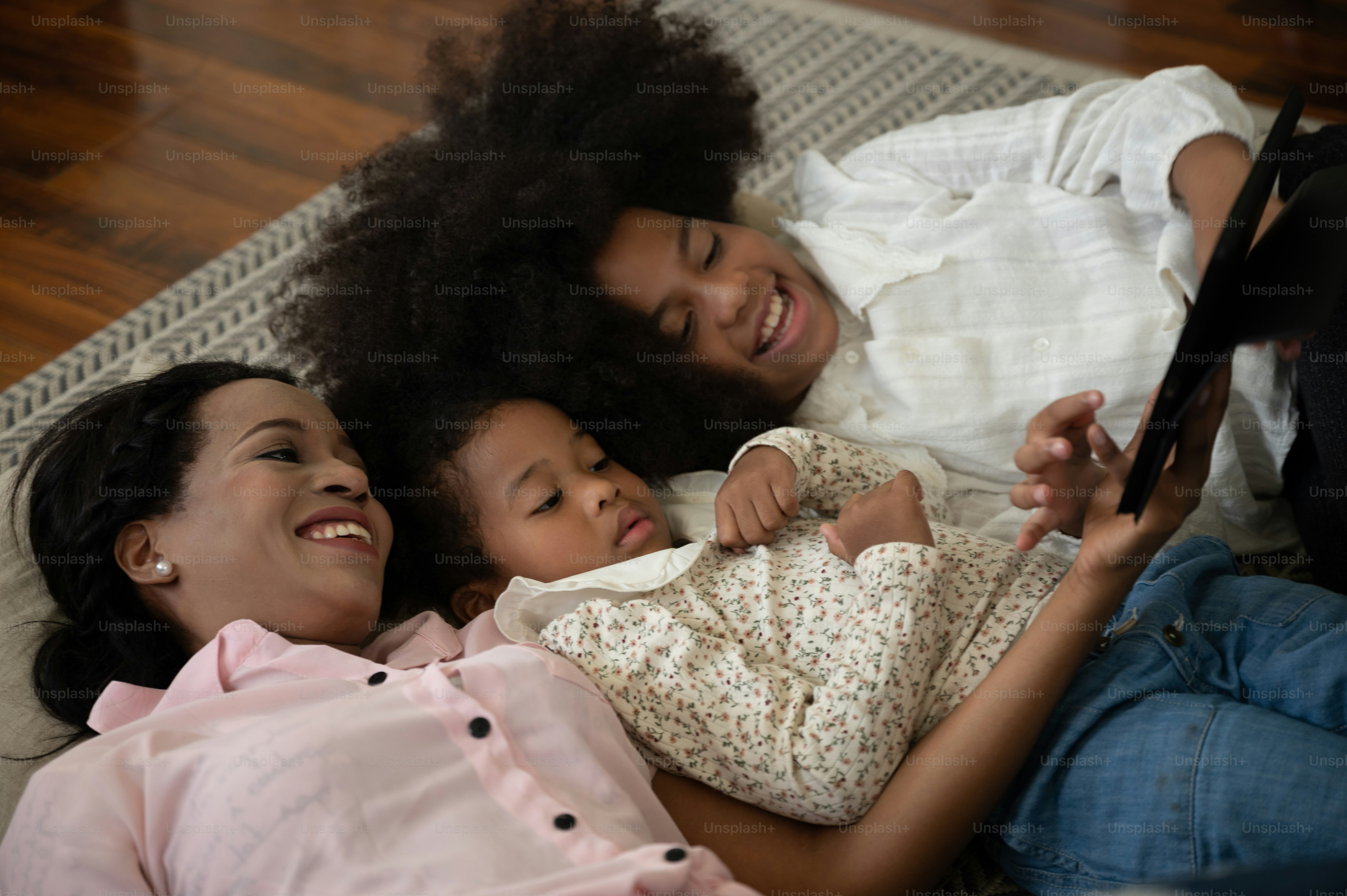 A woman and two children lying on a rug looking at a tablet