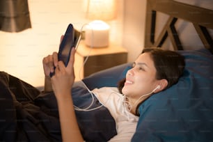 젊은 여성이 태블릿을 사용하여 침실에서 친구나 가족에게 영화 또는 화상 통화를 하고 있습니다.