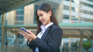 Une jeune femme d’affaires vêtue d’un costume noir utilise un téléphone intelligent, dans la ville, Business Lifestyle Concept.