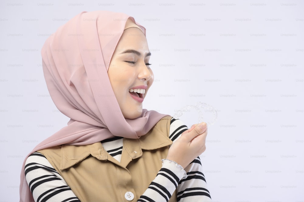 A young muslim woman holding invisalign braces in studio, dental healthcare and Orthodontic concept..