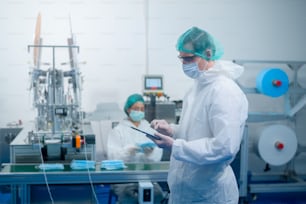 Lavoratori che producono maschere chirurgiche in una fabbrica moderna, protezione Covid-19 e concetto medico.