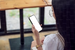 Back view of a woman wearing glasses holding a smartphone blank white screen at the office.