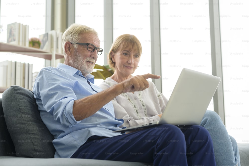 Feliz pareja de ancianos caucásicos usando computadora portátil en casa